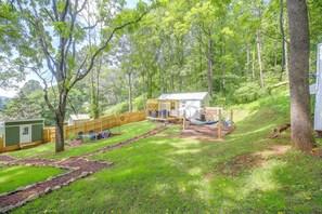 Ein umzäunter Garten mit einer Holzterrasse, einem kleinen Schuppen und einer Hängematte.