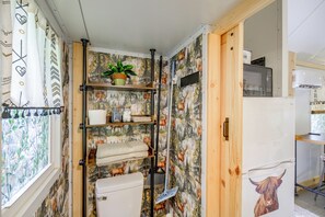 A compact bathroom with a shower, a toilet, and a shelf with toiletries.
