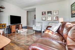 A living room with a leather sofa, a glass coffee table, a television, and framed pictures on the wall. - 5 Mi to Honky Tonk Hwy! Charming Escape w/ Porch (Nashville)