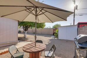 Eine Terrasse mit einem runden Holztisch, zwei Stühlen, einem großen Sonnenschirm und einem Grill.