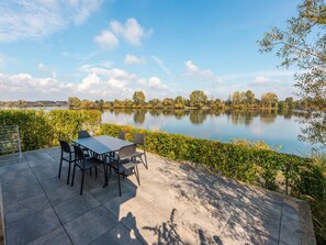 Un patio con mesa y sillas con vista a un lago tranquilo, rodeado de árboles y follaje.