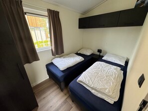 Una habitación pequeña y funcional con dos camas individuales, una ventana con cortinas y suelo de madera.