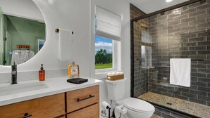 Un baño moderno con tocador blanco, cajones de madera, un espejo redondo, inodoro con función bidé y zona de ducha con puerta de vidrio.