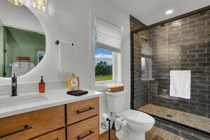 Un baño moderno con tocador blanco, cajones de madera, un espejo redondo, inodoro con función bidé y zona de ducha con puerta de vidrio.