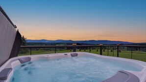 Un jacuzzi en un balcón con vistas a montañas y un cielo despejado.