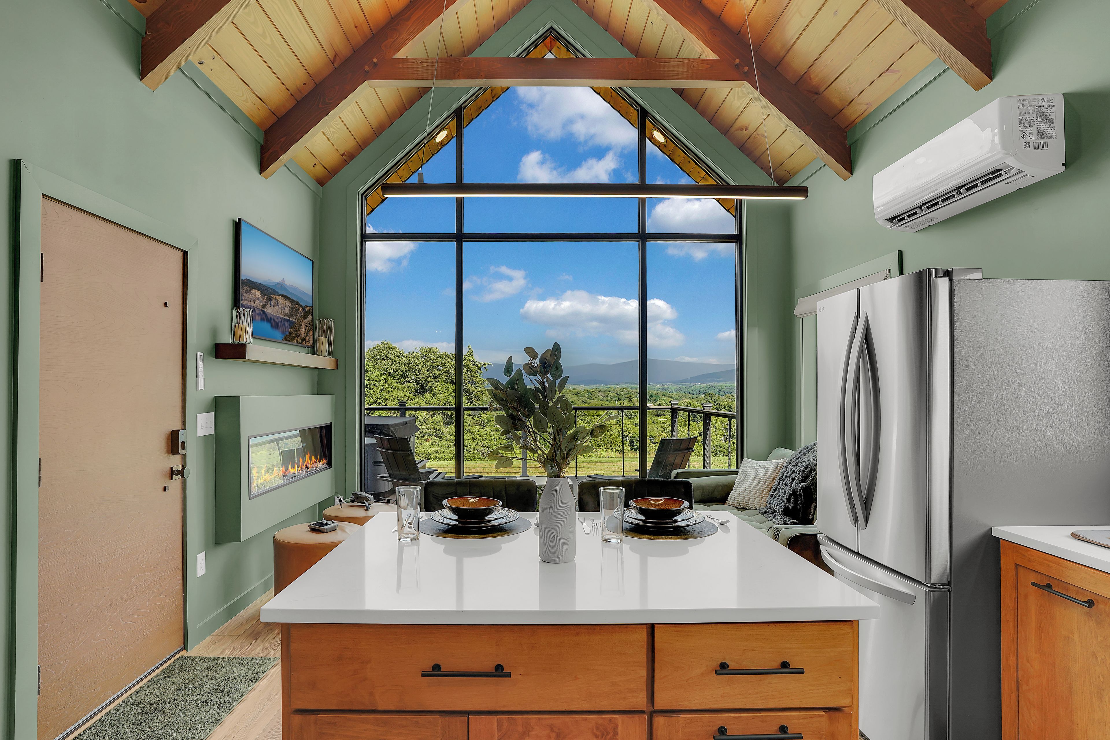 A kitchen with a large window, wooden ceiling, and a modern refrigerator.