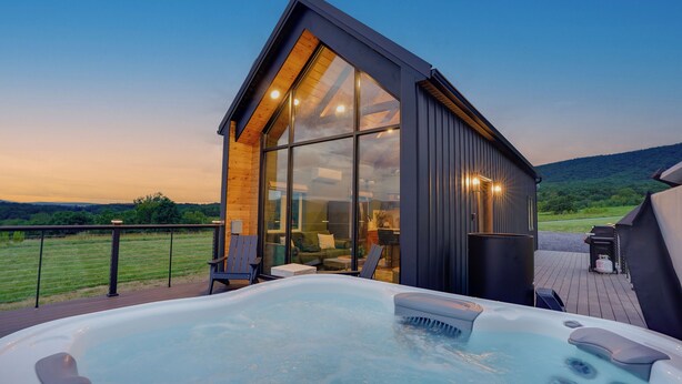 Un edificio moderno con fachada de vidrio, un jacuzzi y una terraza con vistas a un campo cubierto de césped.