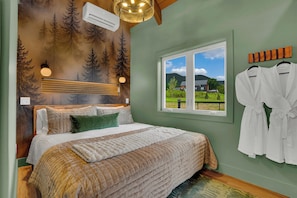 Un dormitorio con una cama grande, un ventanal con vista a una casa y una pared con un mural de un bosque.