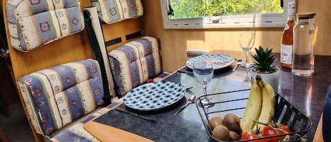 A dining area with patterned seating, a table with a plate, a glass, and a fruit basket.