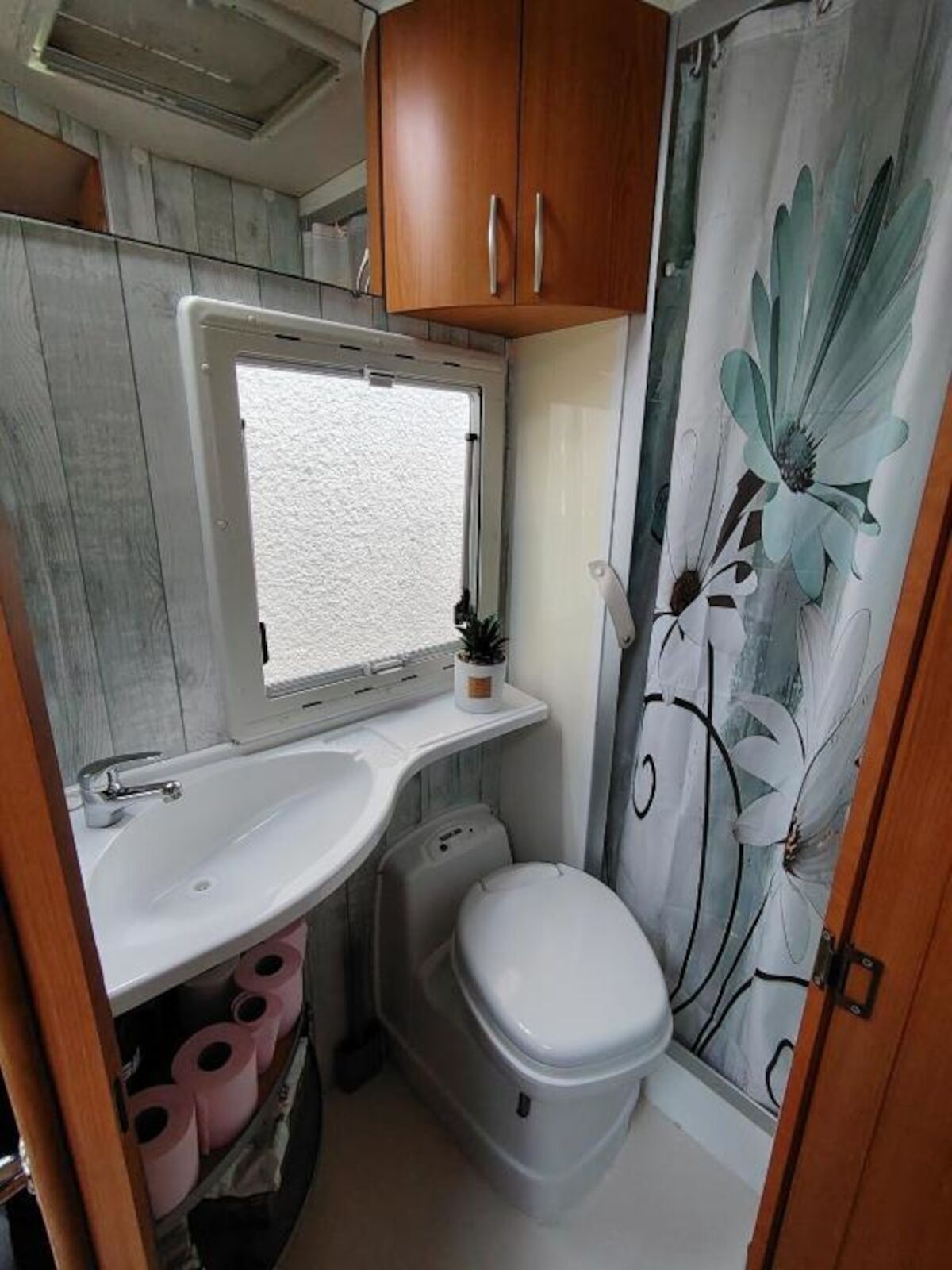 Un baño pequeño con un lavamanos blanco, un inodoro y una cortina de ducha con diseño floral.