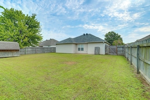 A residential backyard with a house, a wooden fence, and a grassy lawn.