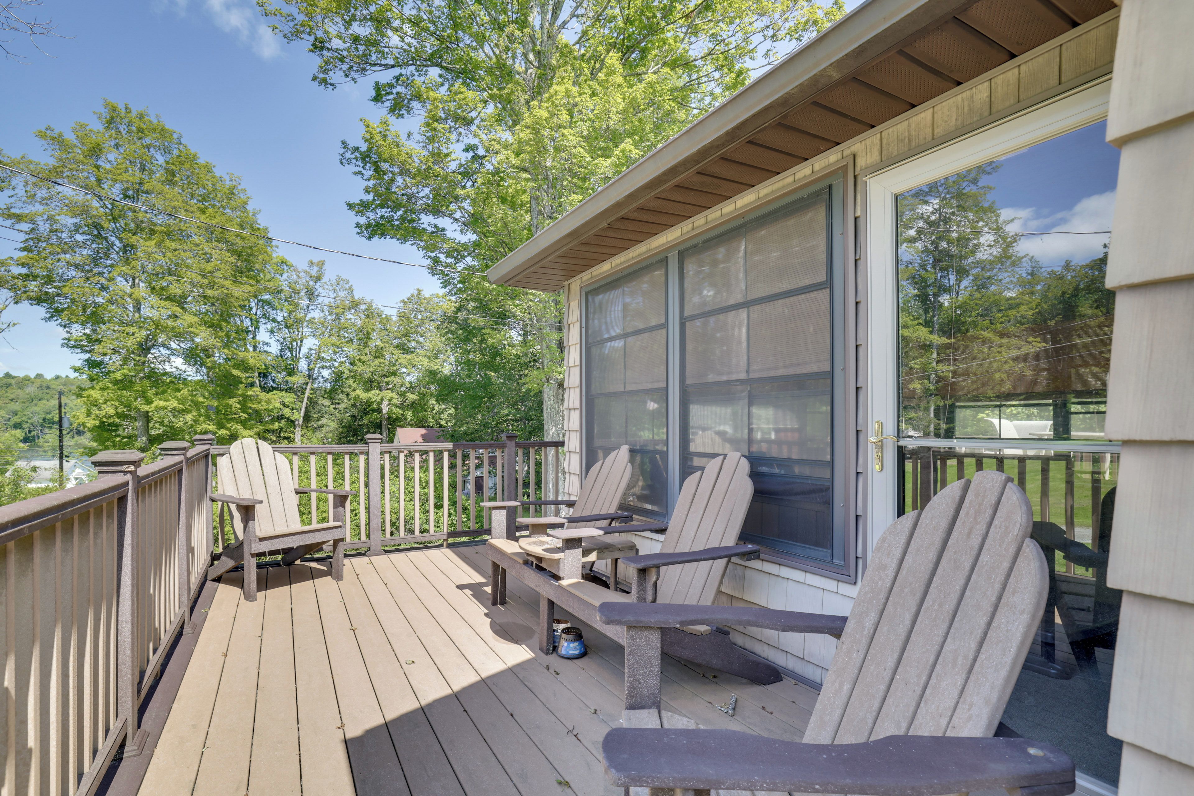 A wooden deck with Adirondack chairs and a table, overlooking a forested area.