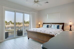 Ein Schlafzimmer mit einem großen Bett, zwei Nachttischlampen, einem Deckenventilator und Blick auf Palmen durch eine Schiebetür.
