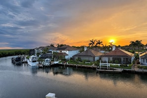 Ein Yachthafen mit Häusern und Booten, eine ruhige Wasserfläche und ein Sonnenuntergang im Hintergrund.