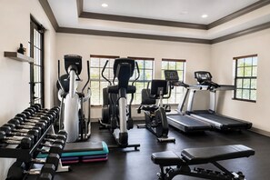 Ein Fitnessstudio mit unterschiedlichen Trainingsgeräten, darunter Laufbänder, Crosstrainer und Kurzhanteln.