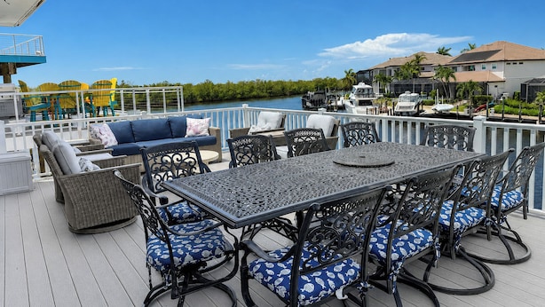 Una terraza con mobiliario exterior, una mesa y sillas, con vista a un cuerpo de agua y una zona residencial.