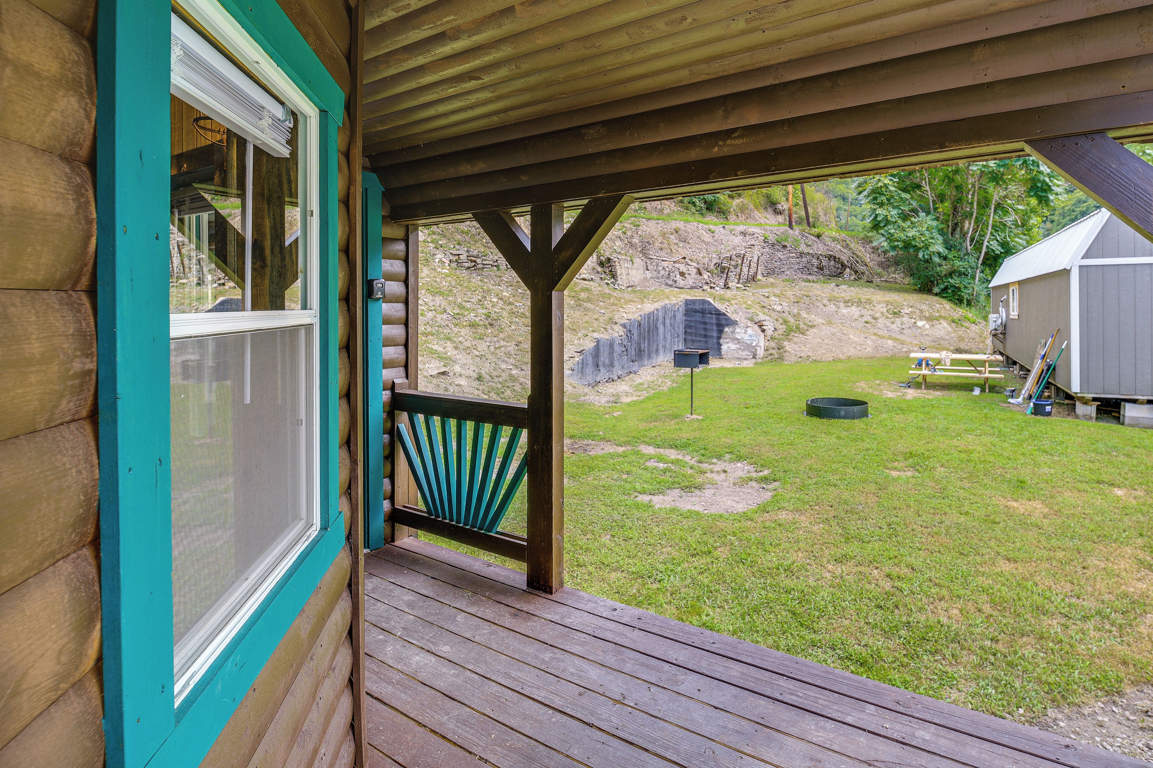 A wooden deck with a view of a grassy yard and a stone wall.
