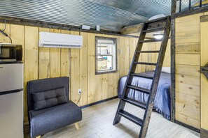 A compact room with a bunk bed, a chair, a microwave, and an air conditioning unit.