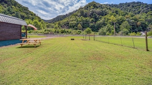 Un área de picnic con mesa y bancos de madera, un refugio techado y vistas a una ladera boscosa.