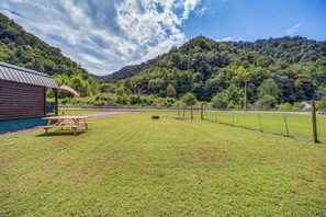 Un área de picnic con mesa y bancos de madera, un refugio techado y vistas a una ladera boscosa.