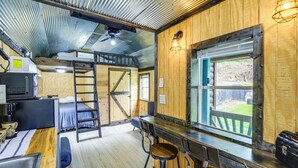Un interior rústico con una litera, una zona de bar con taburetes, una escalera y un ventanal grande.