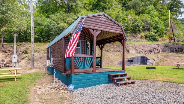 Una pequeña cabaña de madera con un porche, una bandera estadounidense y una mesa de picnic.