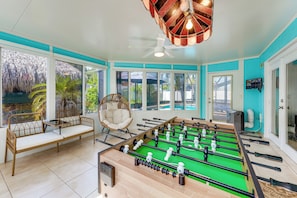 A room with a foosball table, a wicker chair, and a large window overlooking a pool. - 2 Mi to Redington Beach! Tropical Poolside Retreat (Seminole)