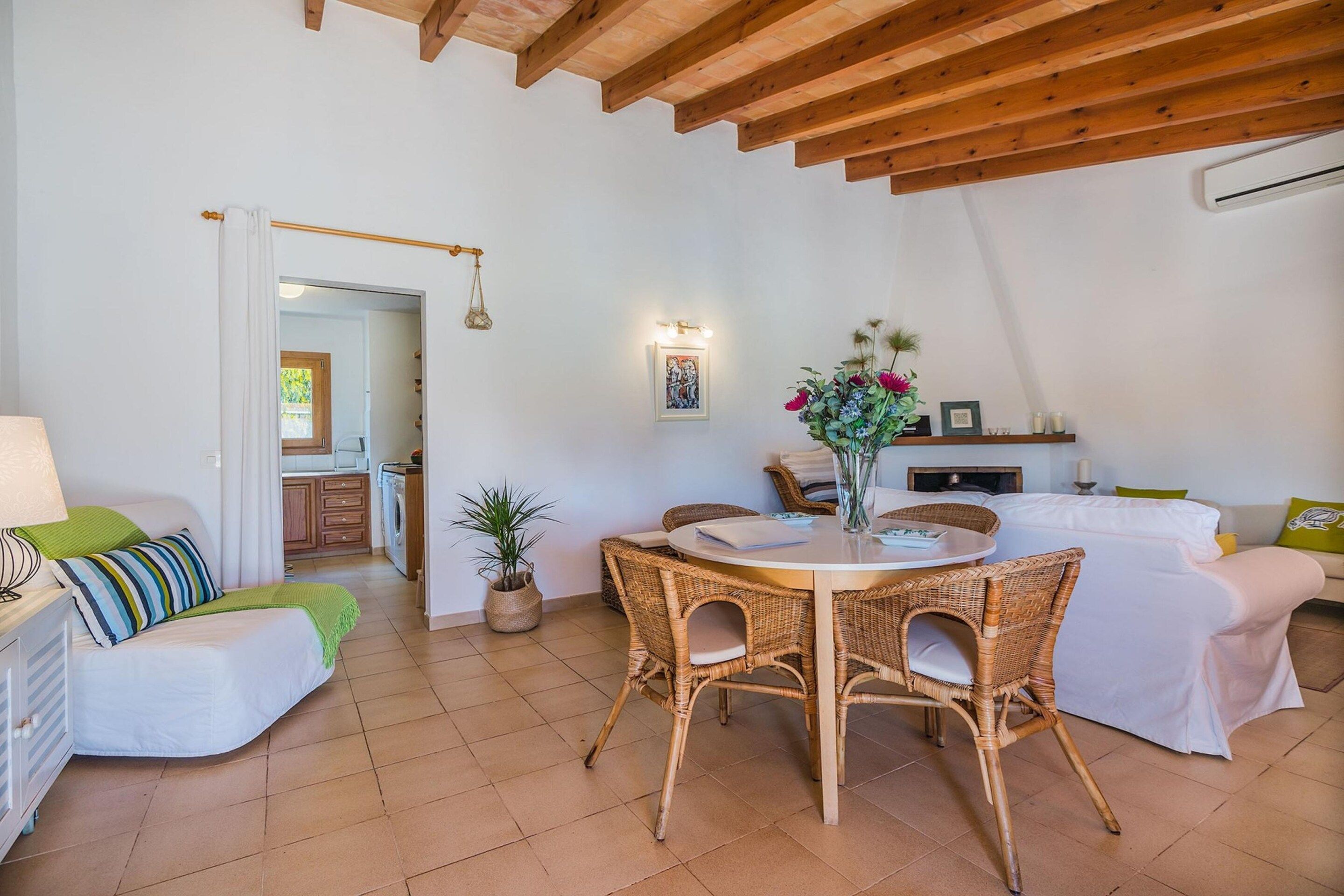 A cozy living area with a dining table, wicker chairs, a sofa, and a kitchen in the background.