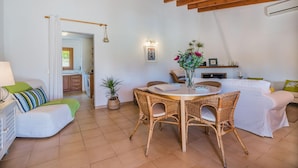 A cozy living area with a dining table, wicker chairs, a sofa, and a kitchen in the background. - Idyllic Country Getaway for 2 (Pollença)