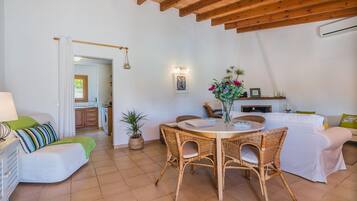 A cozy living area with a dining table, wicker chairs, a sofa, and a kitchen in the background.