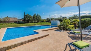 A rectangular swimming pool with a clear blue water surface, surrounded by a concrete deck. There are lounge chairs with green towels, a small white structure, and a large umbrella providing shade. - Idyllic Country Getaway for 2 (Pollença)