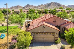 A residential area with a house featuring a red-tiled roof, a garage, and a well-maintained lawn. - Resort-Style Goodyear Home: Swim, Soak & Play! (Goodyear)