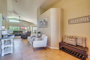 A spacious living room with a sofa, a bench, and a wall-mounted welcome sign. - Resort-Style Goodyear Home: Swim, Soak & Play! (Goodyear)
