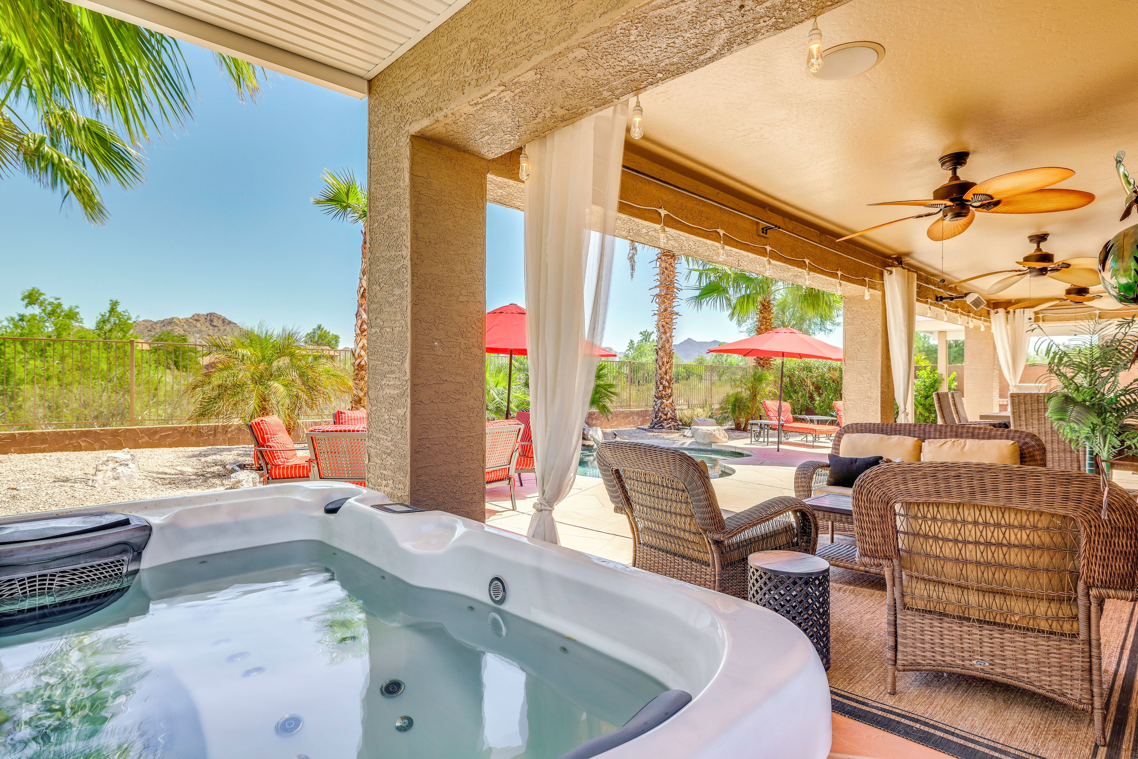 Ein Whirlpoolbereich mit Korbmöbeln, einem Deckenventilator und Blick auf einen Pool und Berge.