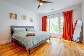 Una camera da letto con un letto, una ventola a soffitto, una finestra con tende e opere d'arte al muro.