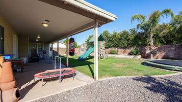 Un área de patio techada con un trampolín, una estructura de juegos y un cielo despejado.