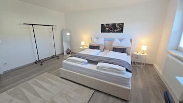 A neatly made bed with pillows and a blanket, a bedside table with a lamp, a large mirror, and a black pull-up bar against the wall.