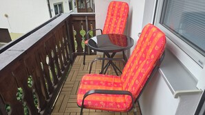 A balcony with a wooden railing, a round table, and two chairs with floral upholstery.