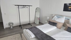 A modern hotel room with a bed, bedside table, lamp, and a full-length mirror. - Vrbo Property (Cham)