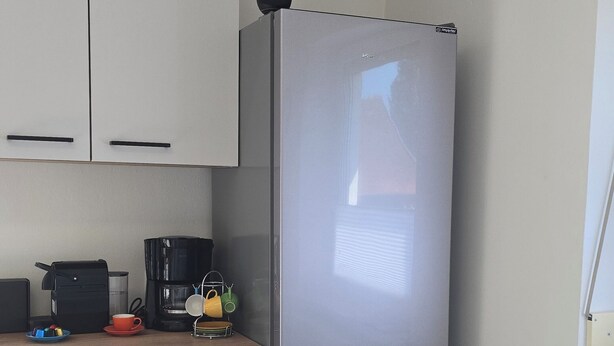A compact kitchen with a stainless steel refrigerator, white cabinets, a wooden countertop, and a dining table.
