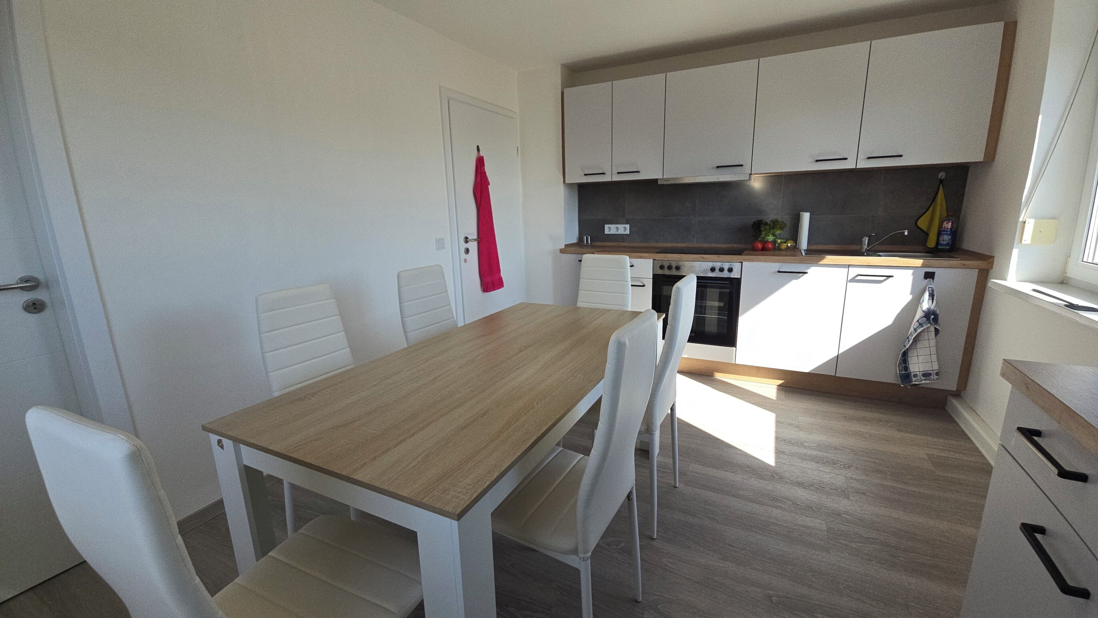 Eine kleine Küche mit weißen Schränken, einem Holztisch und Stühlen.