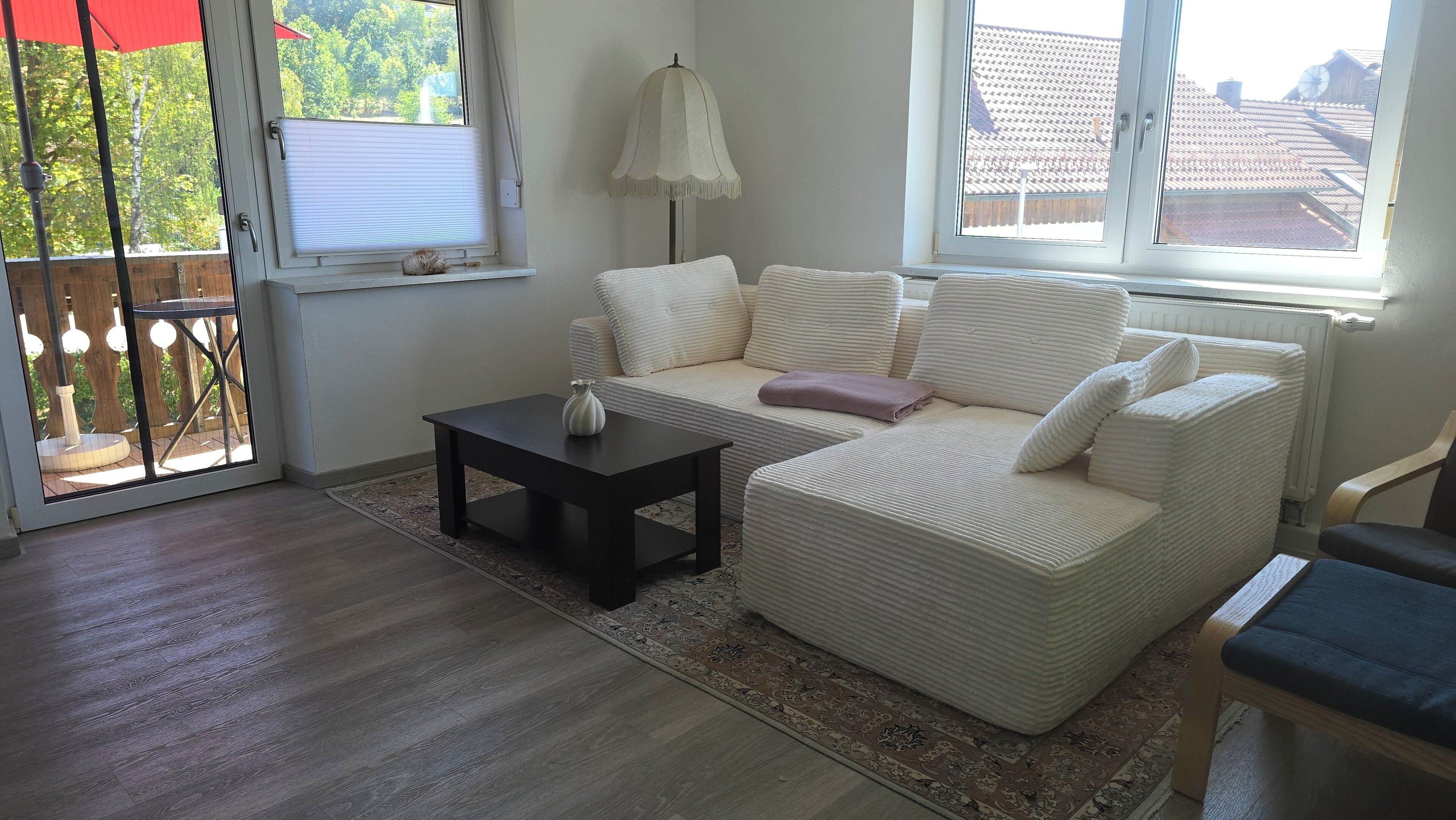 A living room with a sofa, a small table, and a lamp. There is a view of the outside through a window.