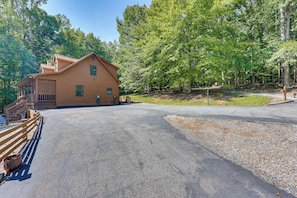 A two-story log cabin with a porch and a driveway leading to a gravel area.