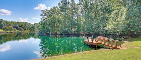 A tranquil lakeside setting with a wooden dock extending into the water, surrounded by lush greenery.