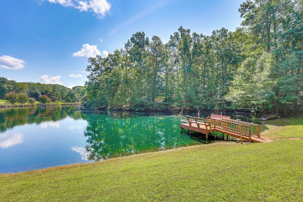 A tranquil lakeside setting with a wooden dock extending into the water, surrounded by lush greenery. - Fishing Dock & Sauna! Farmville Gem w/ Views (Farmville)