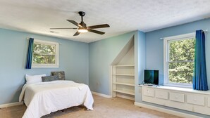 Ein Schlafzimmer mit einem Bett, einem Deckenventilator, einem Fenster mit Vorhängen und einer eingebauten TV-Konsole.