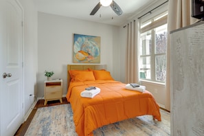 A bedroom with a bed, a nightstand, a painting, and a window with curtains. - Kyle Home at Plum Creek Golf Course (Kyle)