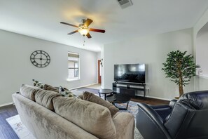 A living room with a sofa, a television, a ceiling fan, and a potted plant. - Kyle Home at Plum Creek Golf Course (Kyle)