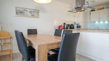 Un comedor con mesa de madera y sillas negras, una lámpara colgante roja, y una cocina con microondas y hervidor.