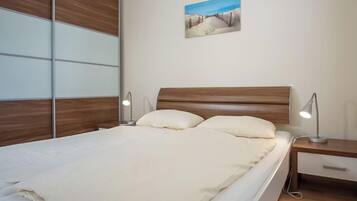 Un dormitorio con cabecera de madera, cama con ropa de cama blanca, dos mesitas de noche con lámparas y un cuadro colgado en la pared.
